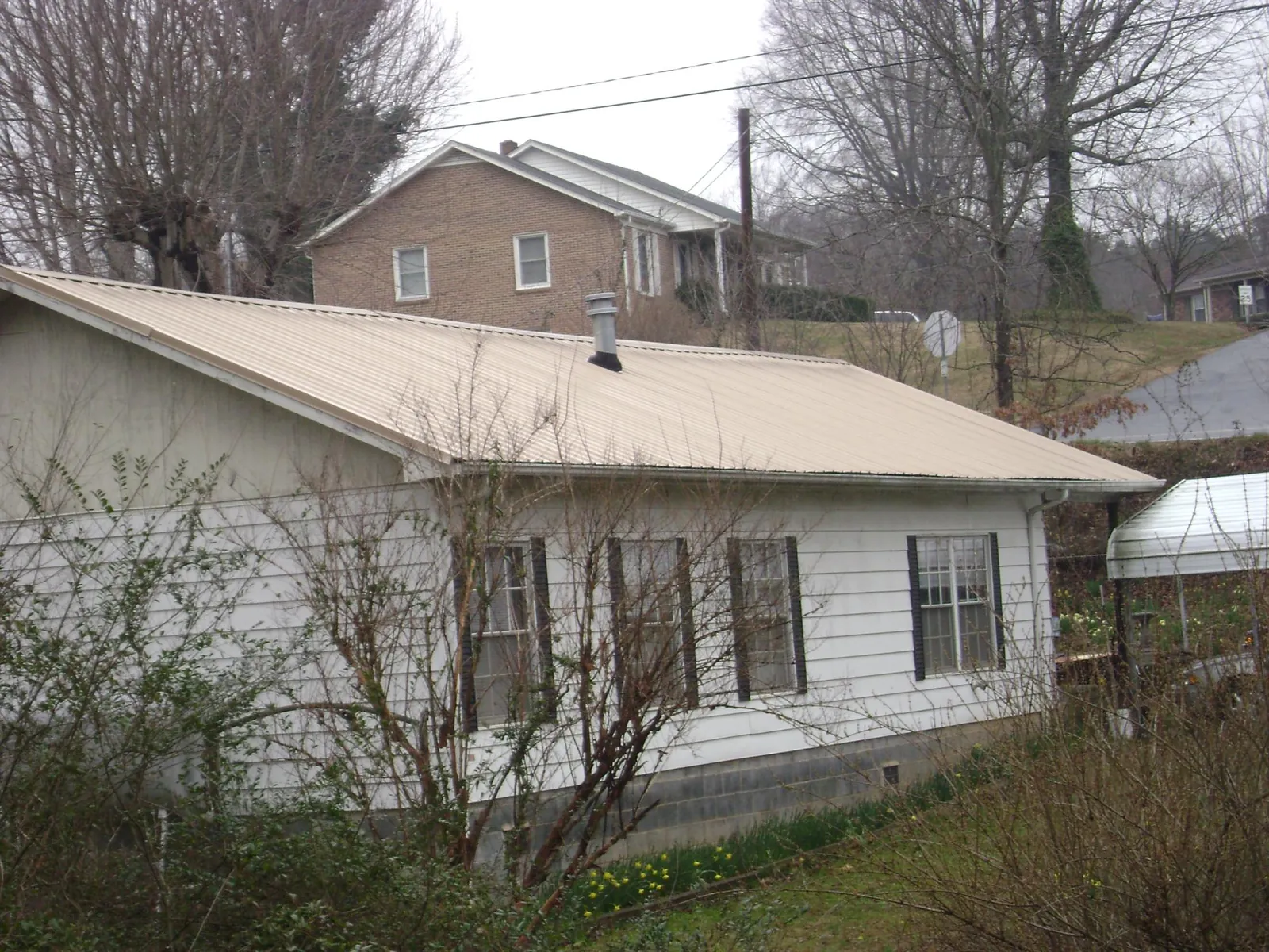 Tan metal roof on a white sided house set into a hillside — Commercial Roofing by Roofing Brothers in Montpelier